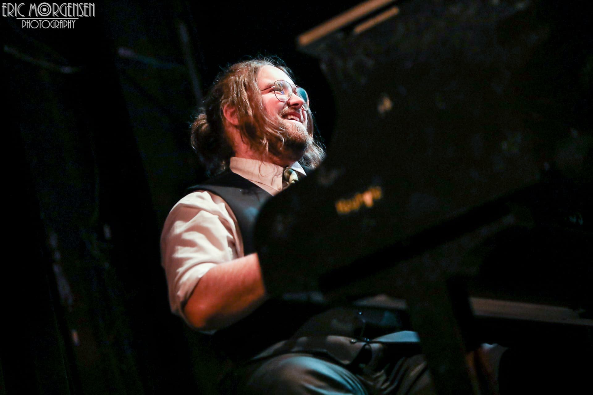 Grant Larcom playing a grand piano under stage lighting